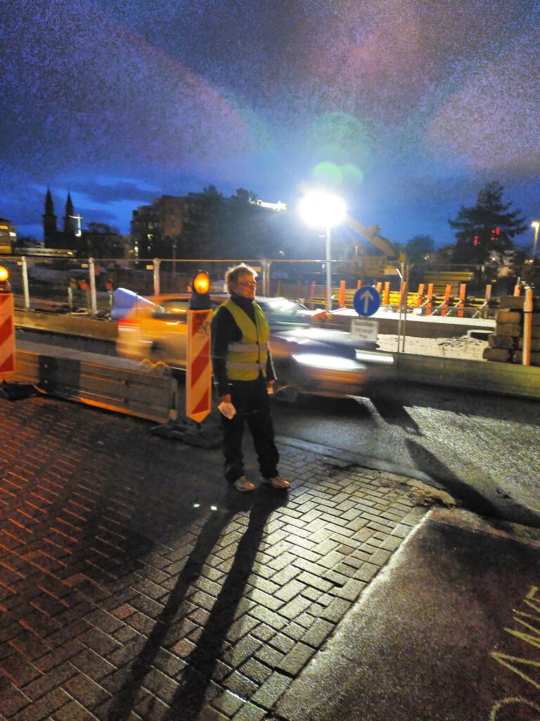 Frau in Warnweste verteilt Muffins an vorbeifahrende